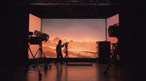 Actors performing in front of a giant, curved virtual production LED wall displaying a detailed alien planet landscape in real-time.